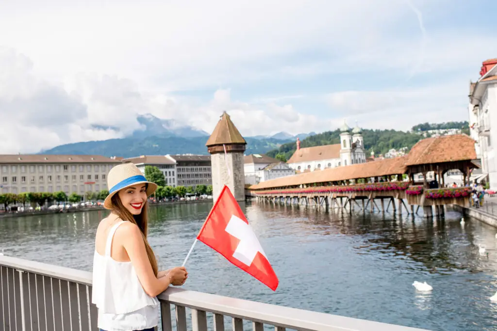 Young female traveler standing with swiss flag in front of the famous wooden bridge in Lucerne city in Switzerland