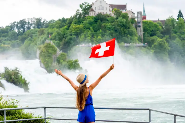 Young female tourist with swiss flag near the famous Rhine waterfall in Switzerland