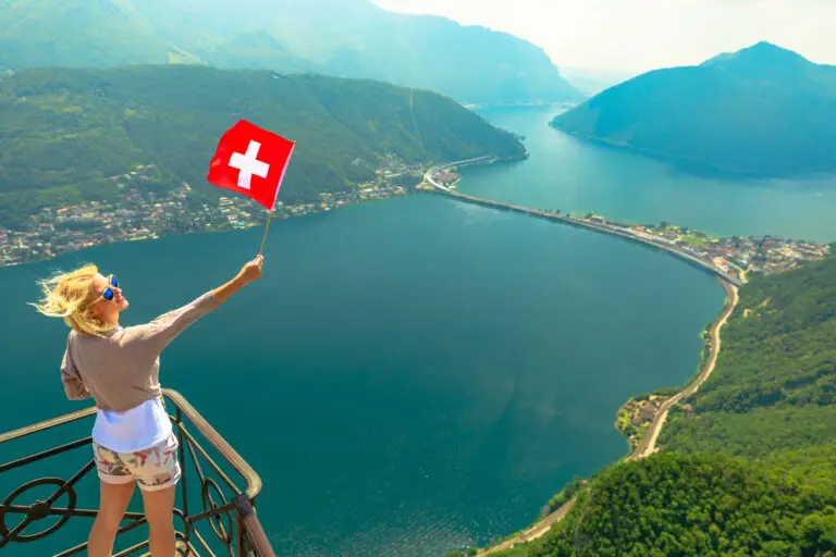 Girl with Swiss flag on top of Lugano skyline from San Salvatore peak in Ticino canton. Lugano Lake in Switzerland. Aerial view lookout from San Salvatore Mount.